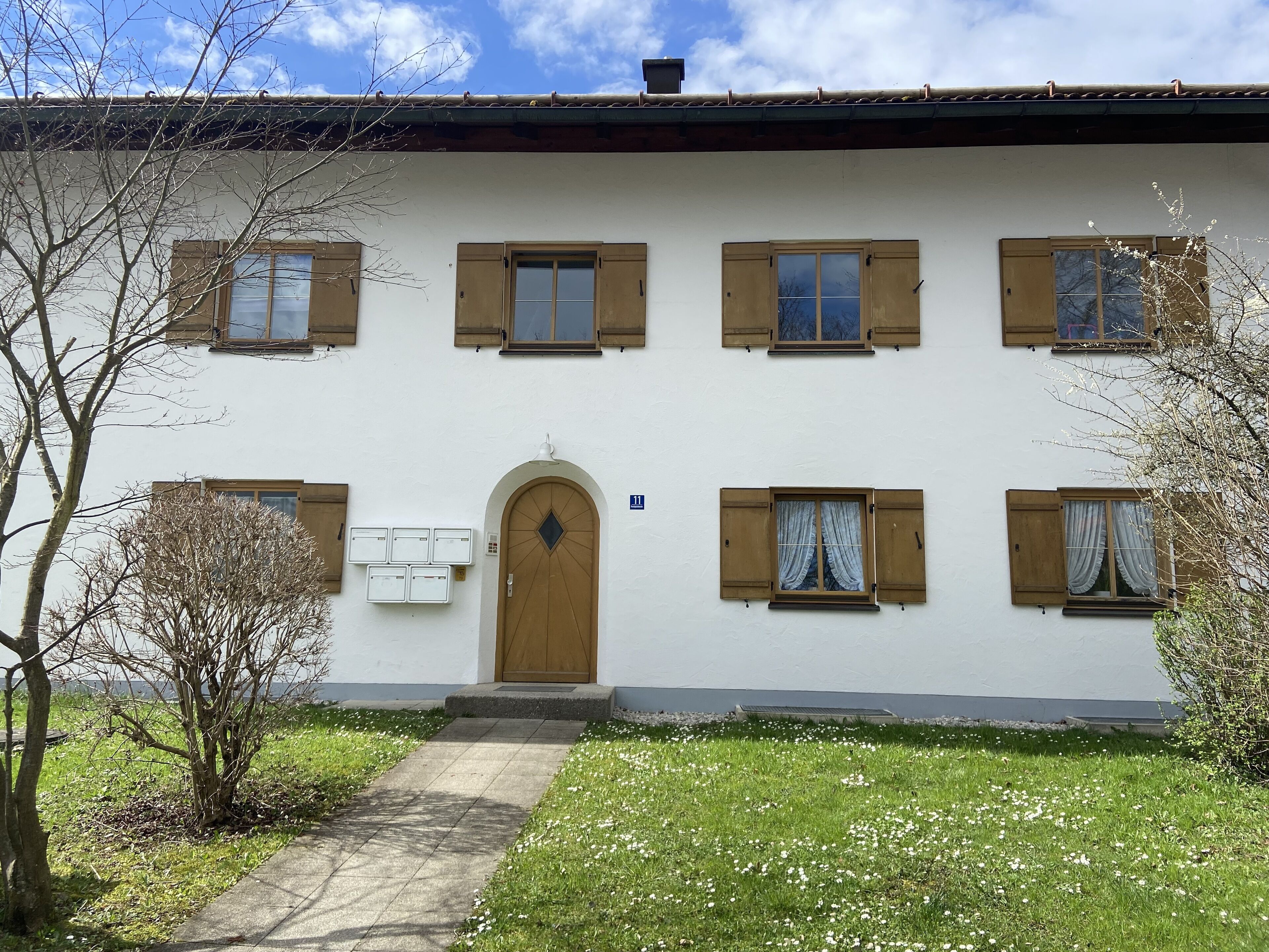 Un edificio a due piani con un ingresso centrale, diverse finestre con persiane e un piccolo giardino antistante.