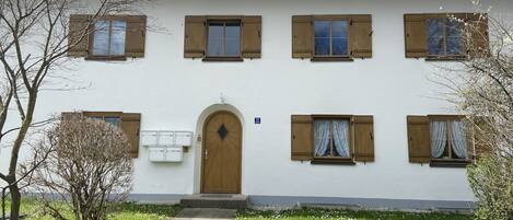 Un edificio a due piani con un ingresso centrale, diverse finestre con persiane e un piccolo giardino antistante.