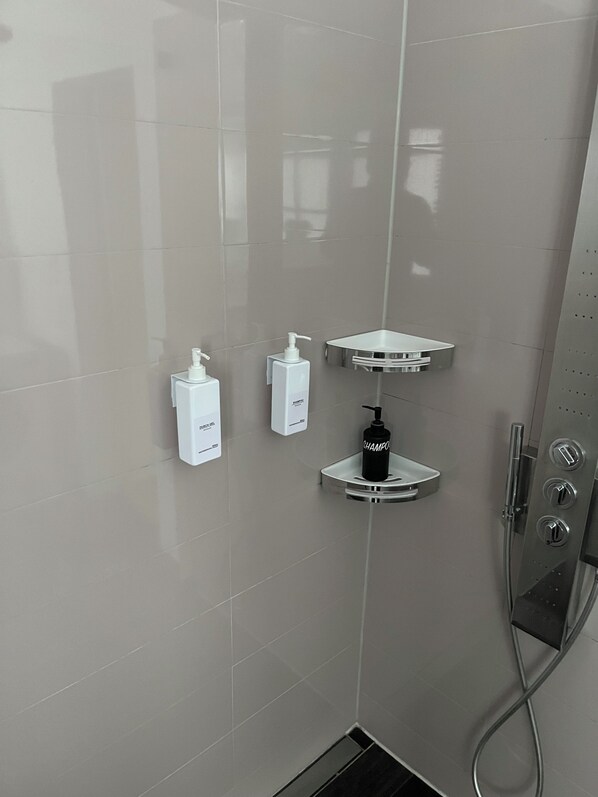 A modern bathroom with a shower, a hand soap dispenser, a shampoo bottle, and a towel rack.