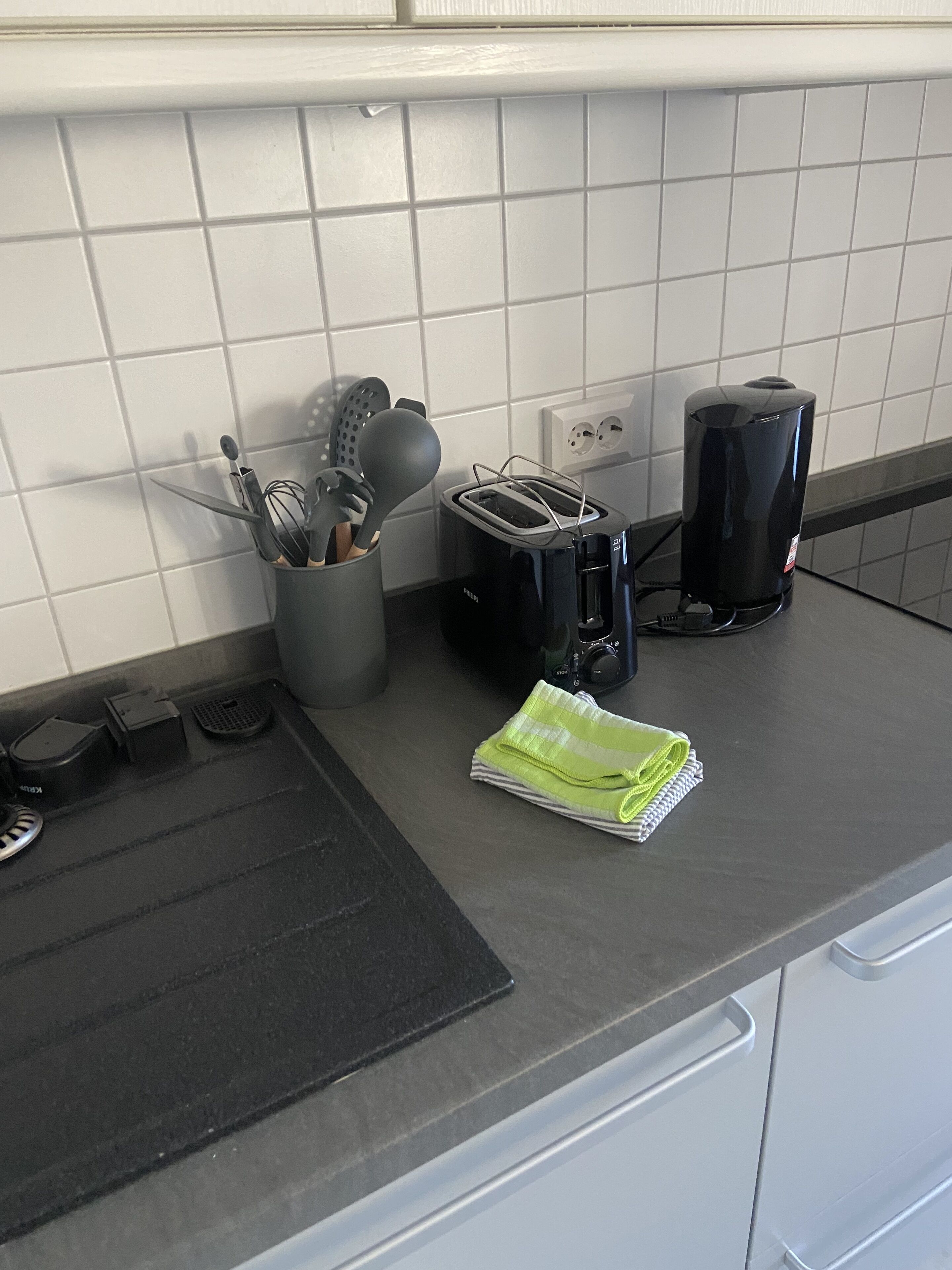 A kitchen counter with a toaster, a coffee maker, a sink, and a utensil holder.