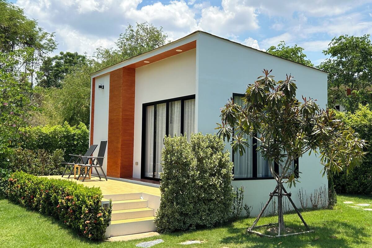 A modern house with a white exterior, a wooden accent wall, and a patio with a chair and a table.