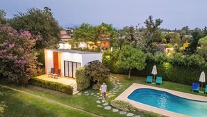 Ein moderner Poolbereich im Freien mit einem kleinen Gebäude, einem Steinweg und üppiger Bepflanzung.