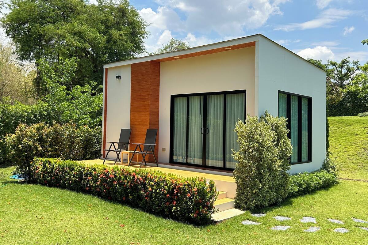 A modern single-story house with a large sliding glass door, a small patio with outdoor furniture, and a well-maintained garden.