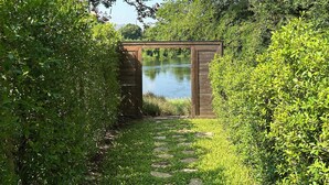 Ein Gartenweg, der zu einer hölzernen Struktur führt, mit einem Teich im Hintergrund.