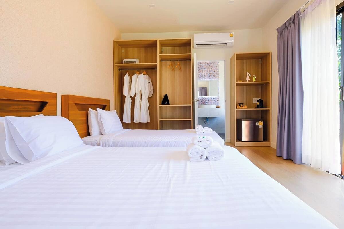 A hotel room with two beds, wooden wardrobes, a mirror, and a minibar.