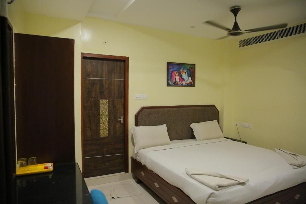 A bedroom with a bed, a wooden wardrobe, a ceiling fan, and a small painting on the wall.