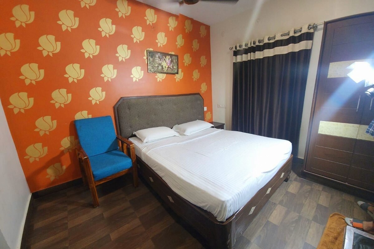 Quarto de hotel com cama, uma cadeira azul, guarda-roupa e parede com padrão floral.