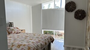 Une chambre à coucher avec un lit, un ventilateur de plafond, de grandes fenêtres et une vue sur l’extérieur.