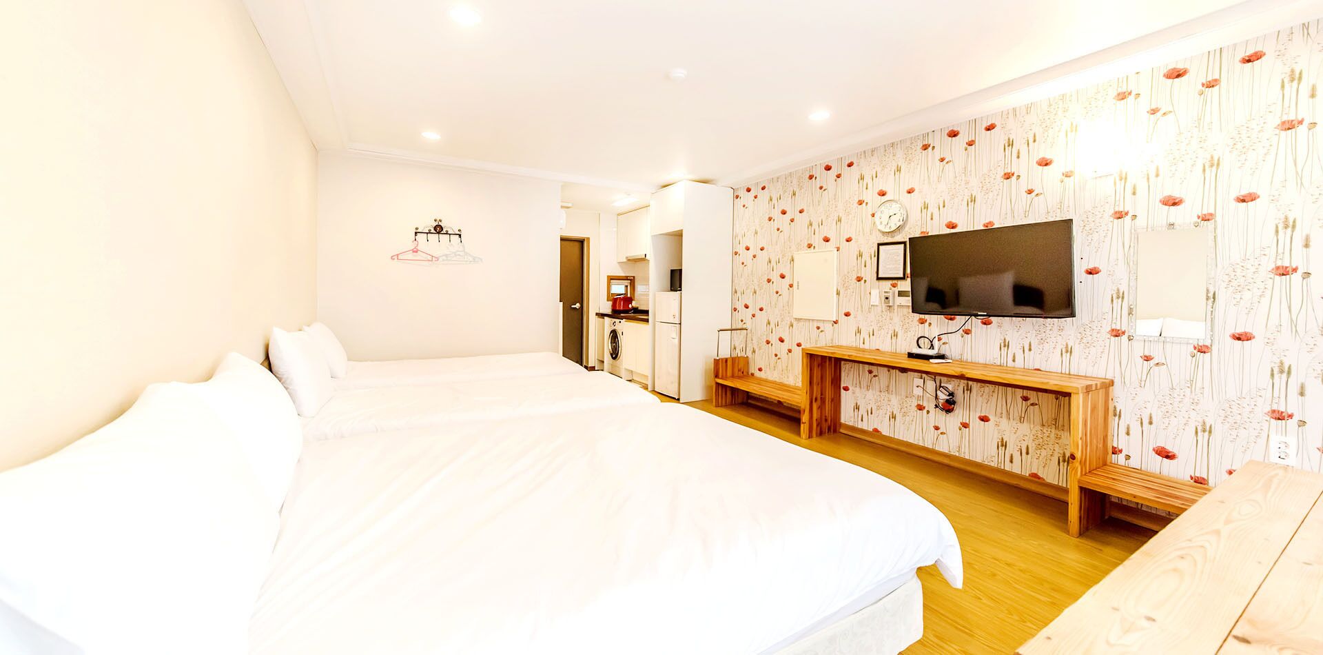 Habitación de hotel con dos camas grandes, un banco de madera, un televisor y una pared con papel tapiz floral.