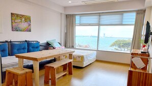 A modern room with a wooden table, blue sofa, and a view of the sea. - Aerang and Baebijang's House (Jeju City)