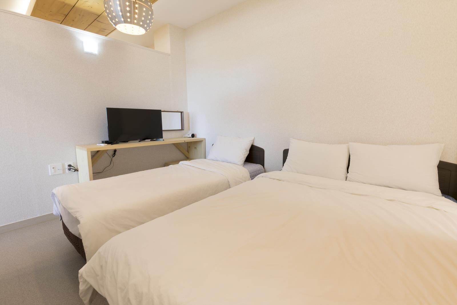 A hotel room with two beds, a TV on a wooden stand, and a ceiling light fixture.