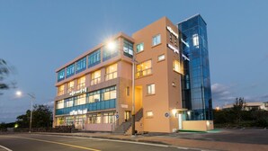 A multi-story building with a coffee shop on the ground floor, a staircase leading to the upper floors, and a glass facade on the right side. - Aerang and Baebijang's House (Jeju City)