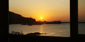 Ein Sonnenuntergangsblick aus einem Fenster auf einen Hafen mit Schiffen und Industriegebäuden.