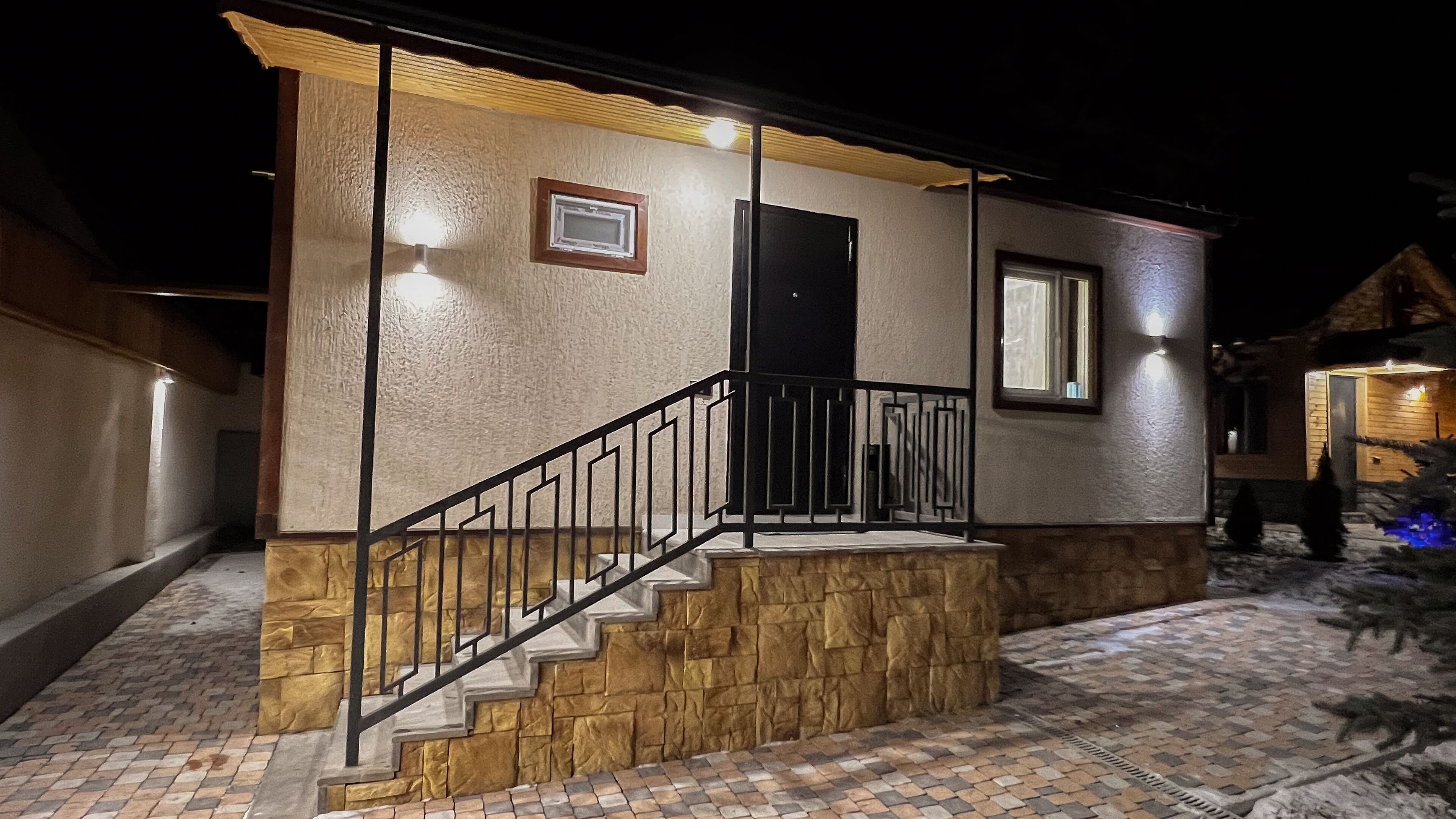 A house with a stone facade, a wooden staircase, and a black railing.