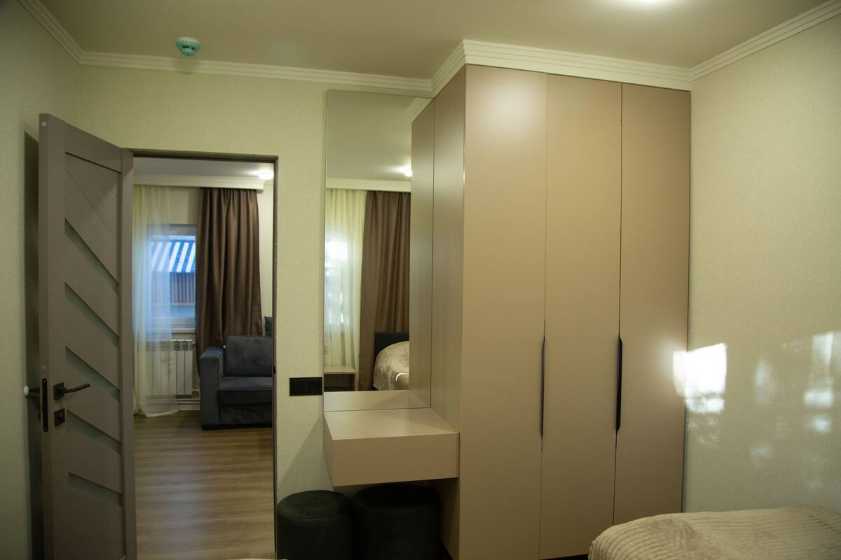 A hotel room with a large wardrobe, a small desk, a bed, and a mirror.