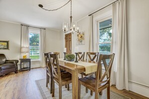 A dining area with a wooden table, chairs, a chandelier, and a view of the outdoors.