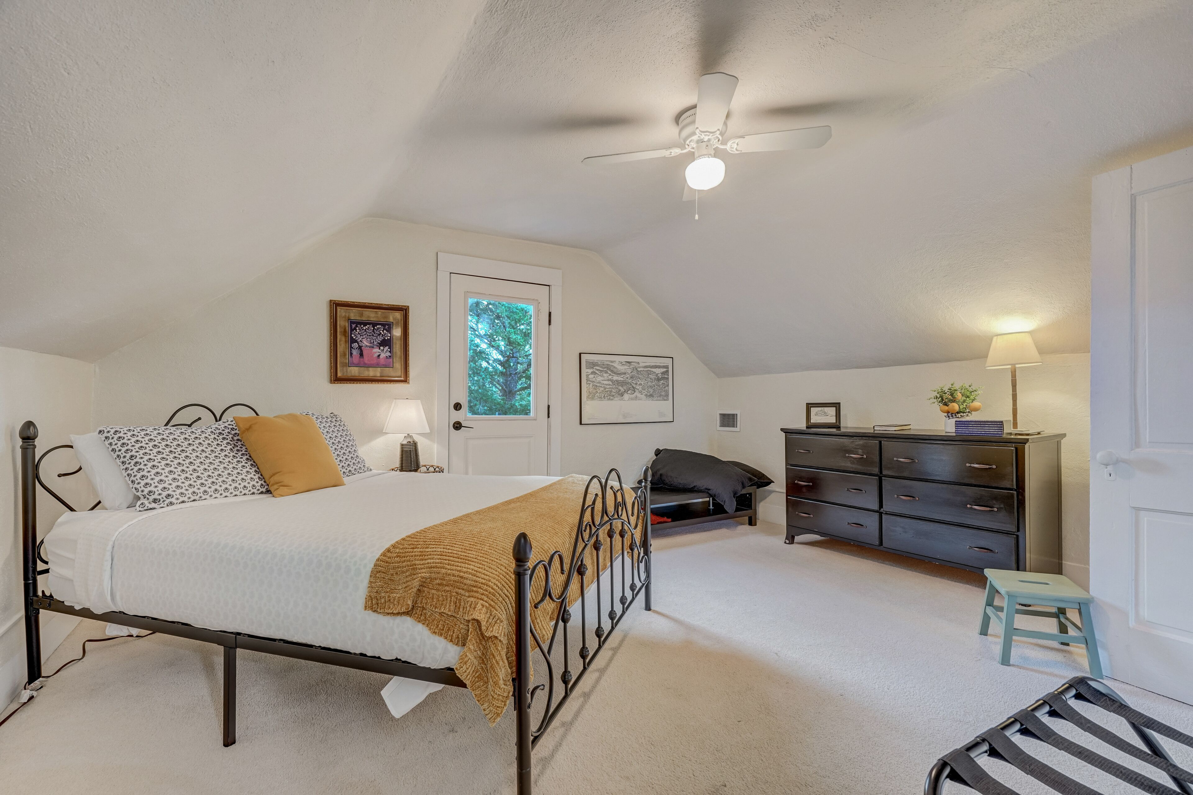 A bedroom with a bed, a dresser, a chair, a ceiling fan, and a door.