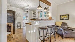 A kitchen with wooden flooring, a bar area with stools, a leather sofa, and pendant lighting. - Bluebird Inn (Monument)