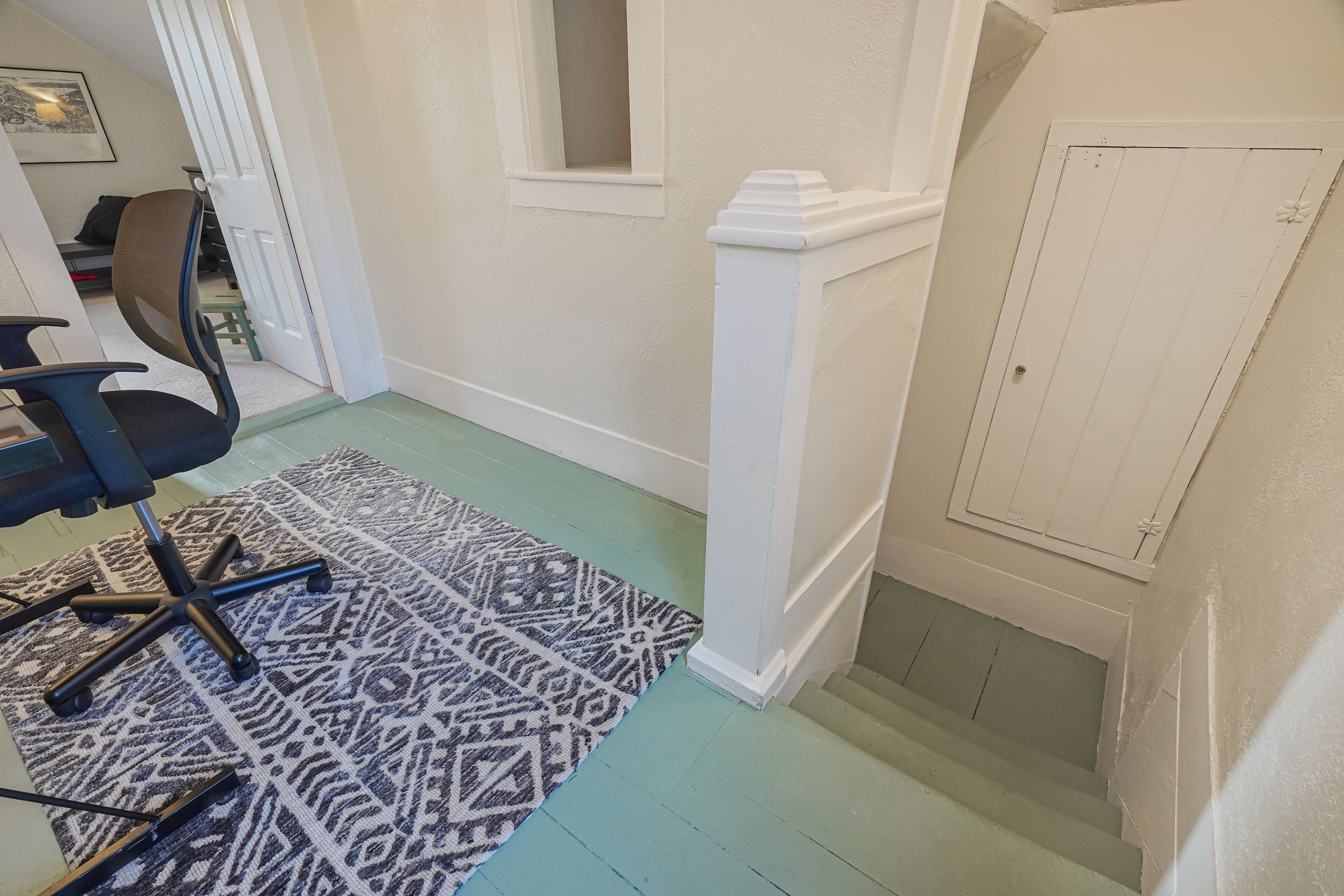 Un couloir avec un tapis à motifs, une chaise et une porte dotée d’une petite fenêtre.