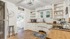 A kitchen with white cabinetry, a wooden countertop, a stove, and a clock on the wall. - Bluebird Inn (Monument)
