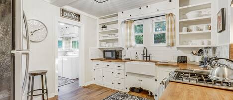 A kitchen with white cabinetry, a wooden countertop, a stove, and a clock on the wall.