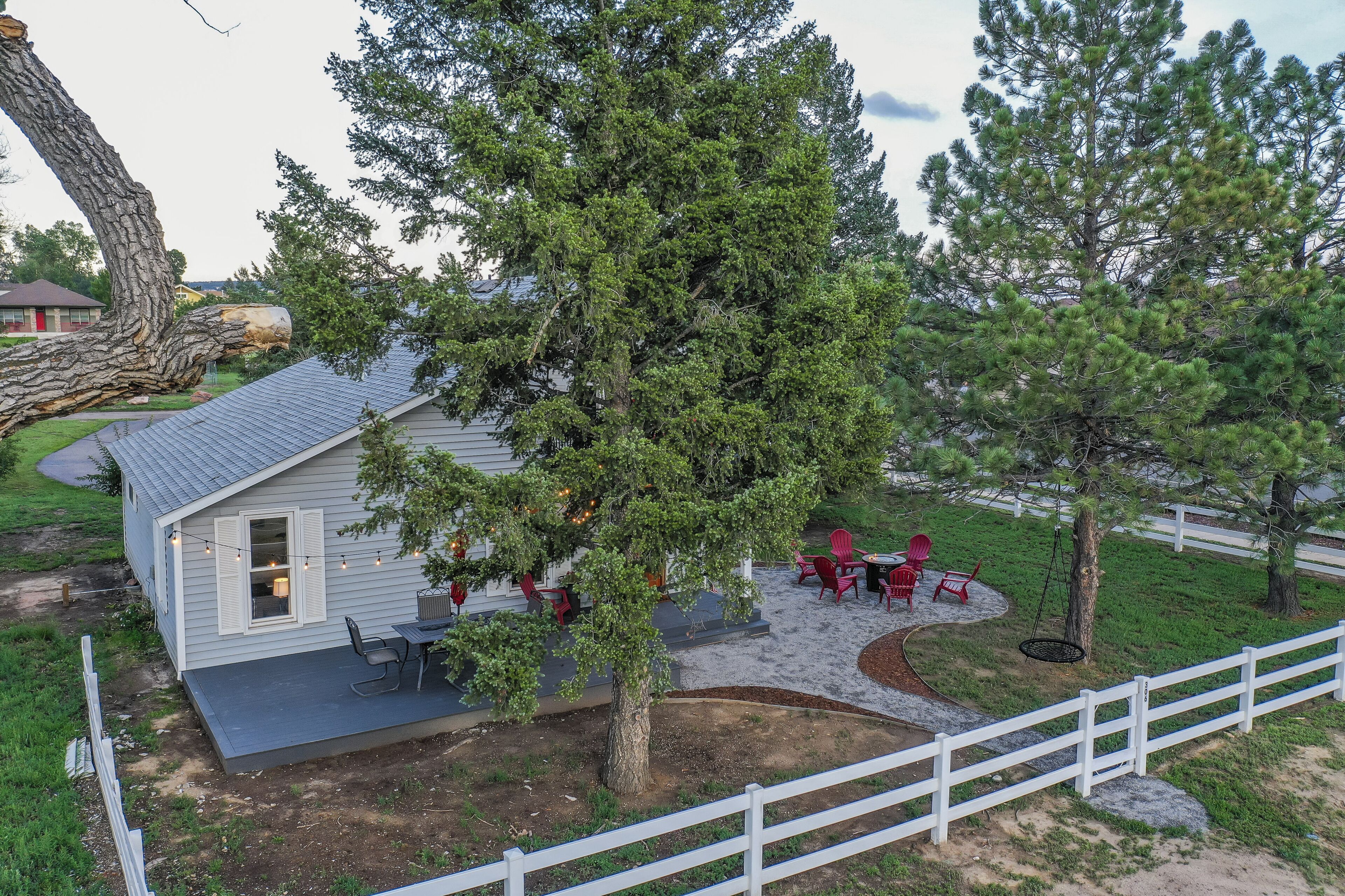 A small house with a patio, outdoor seating, and a large tree.