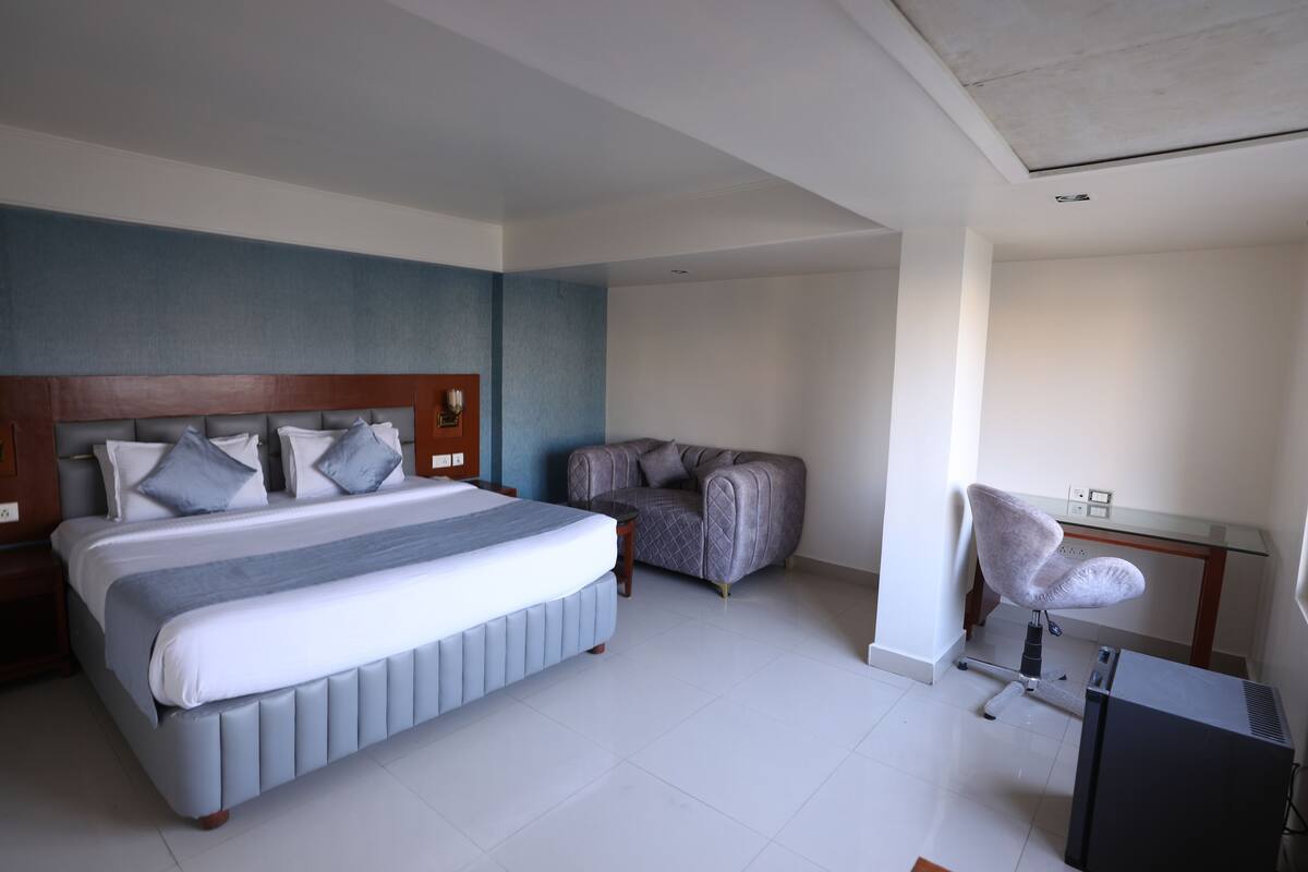 Una habitación de hotel moderna con una cama grande, un sillón gris y un escritorio con una silla.