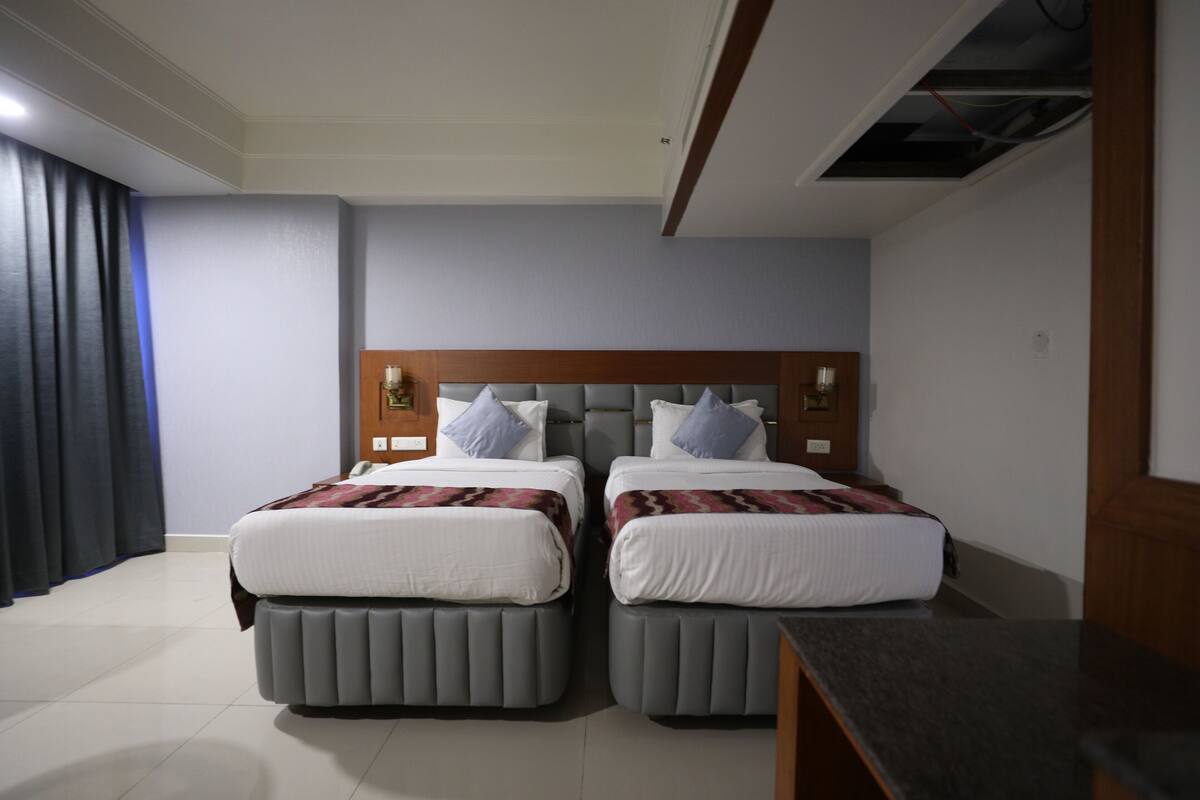 Habitación de hotel con dos camas, cabecero de madera, una mesita y una ventana con cortinas.