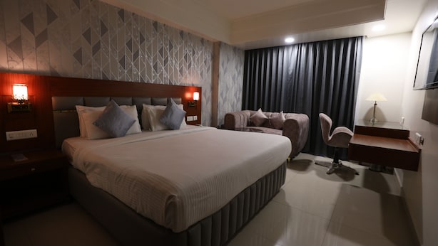 A modern hotel room with a large bed, a desk with a chair, a sofa, and a TV mounted on the wall. - Eastin Hotels (Hyderabad)