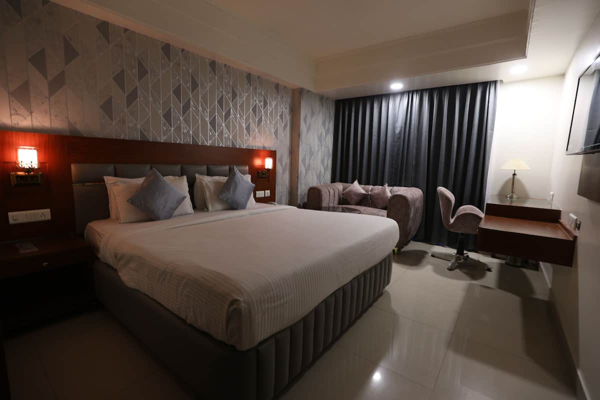 Una habitación de hotel moderna con una cama grande, un escritorio con una silla, un sofá y un televisor montado en la pared.