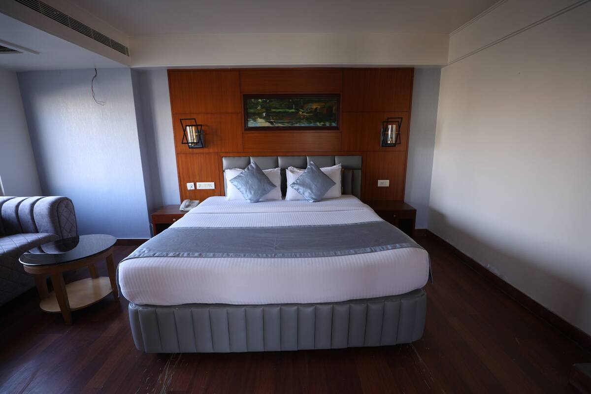 Una cama grande con cabecera gris, dos mesitas de noche, un revistero, una silla y un cuadro en la pared.