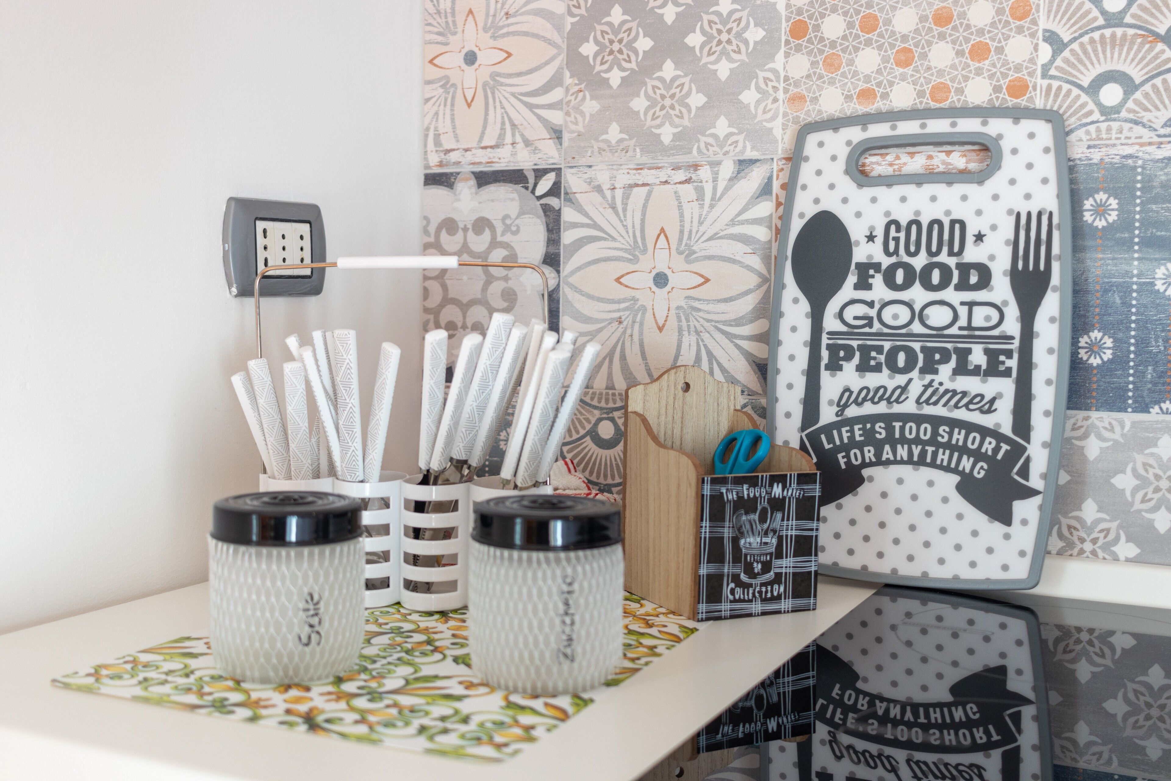 A kitchen counter with utensils, a knife block, a power outlet, and decorative plates with sayings.