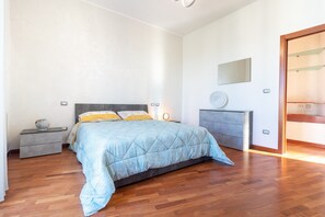Un dormitorio con cama, mesitas de noche, cómoda, espejo y puerta.
