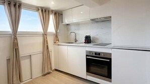 Une cuisine moderne avec des meubles blancs, un pare-feu en marbre, un four encastré et une fenêtre avec des rideaux.