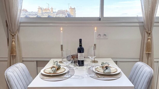 Une salle à manger avec une table dressée pour deux personnes, deux chaises, une bouteille de vin et des bougies.