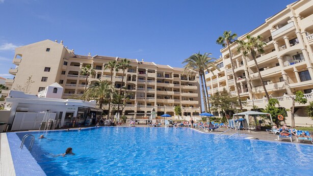 A hotel with a swimming pool, multiple balconies, and palm trees. - Castle Harbour 3 (Los Cristianos)