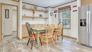 Een keuken met houten kasten, een roestvrijstalen koelkast, een eettafel met stoelen en planken met decoratieve objecten.