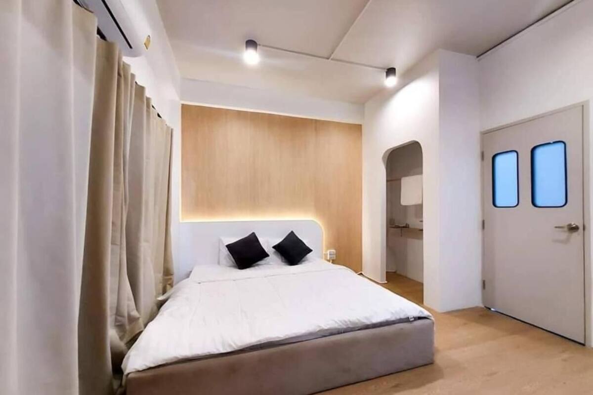 A modern bedroom with a large bed, a wooden headboard, and a door with two windows.