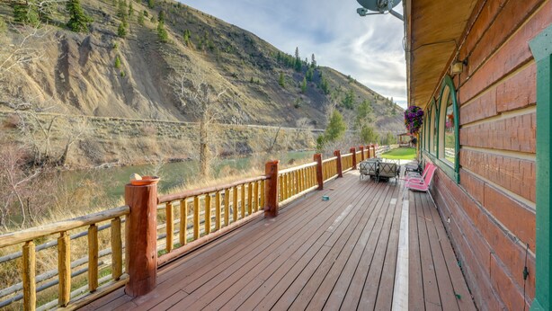 Een houten terras met een reling, met uitzicht op een rivier en bergen.