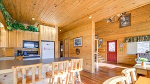 A wooden cabin interior with a kitchen area, wooden bar stools, and a dining table.