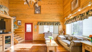 A cozy log cabin interior with a wooden floor, a leather sofa, a wooden coffee table, and a red door.
