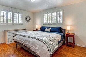 Une chambre à coucher comprenant un lit, deux tables de chevet, une commode et une fenêtre avec des stores.