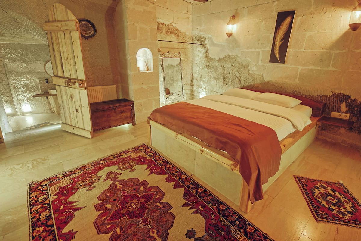 A bedroom with a wooden bed, a stone wall, a wooden bench, and a rug.
