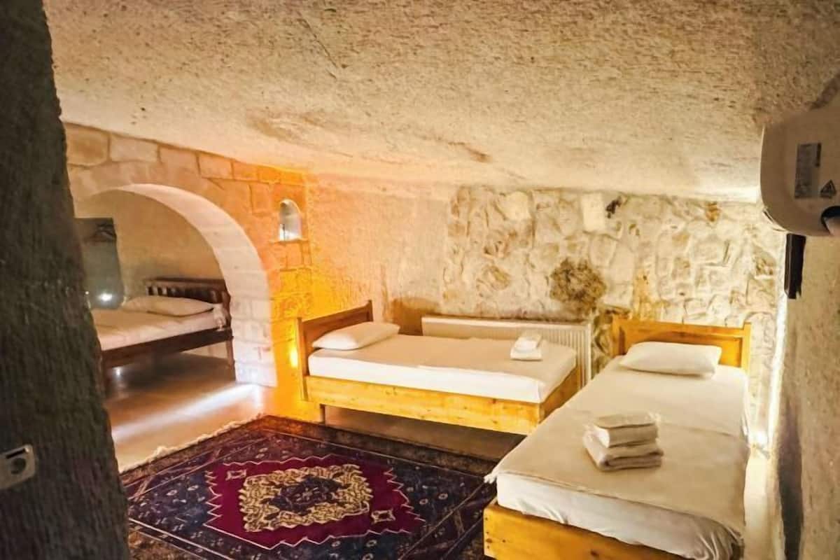 A rustic room with two wooden beds, a stone wall, and a small archway.