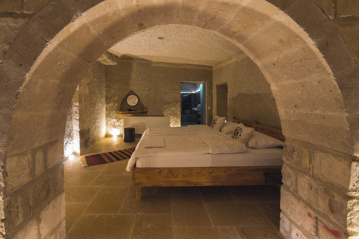A stone-walled bedroom with a wooden bed, a circular skylight, and a stone floor.