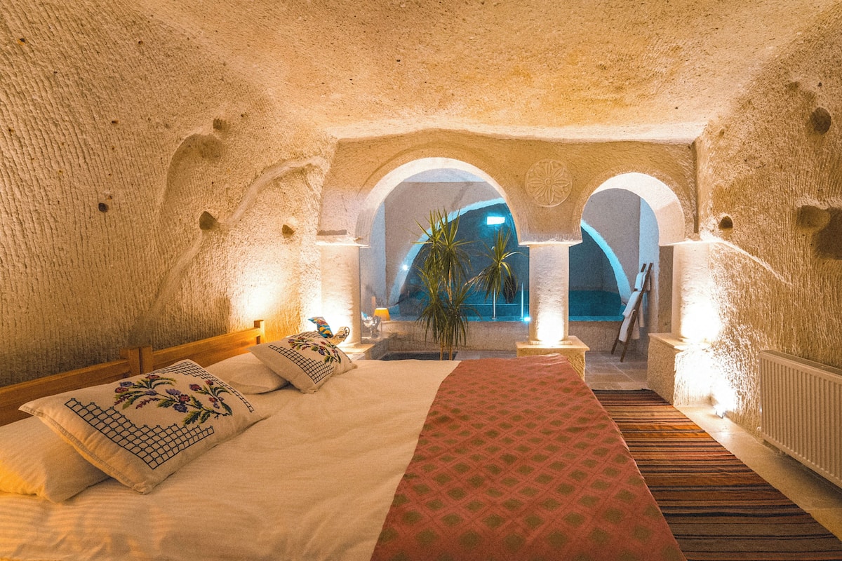 A room with a bed, a red carpet, and a view of a pool through an arched window.