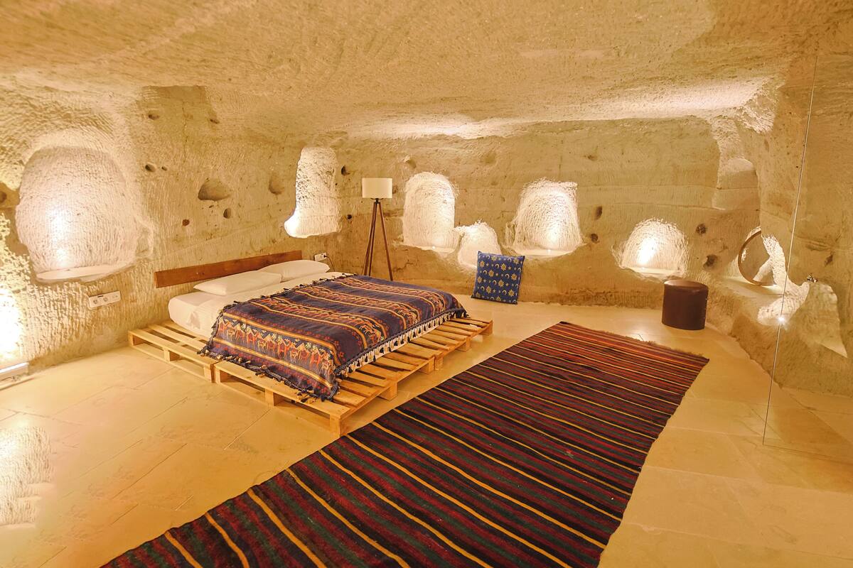 A cozy, cave-like bedroom with a bed, pillows, a bedside lamp, and a rug.
