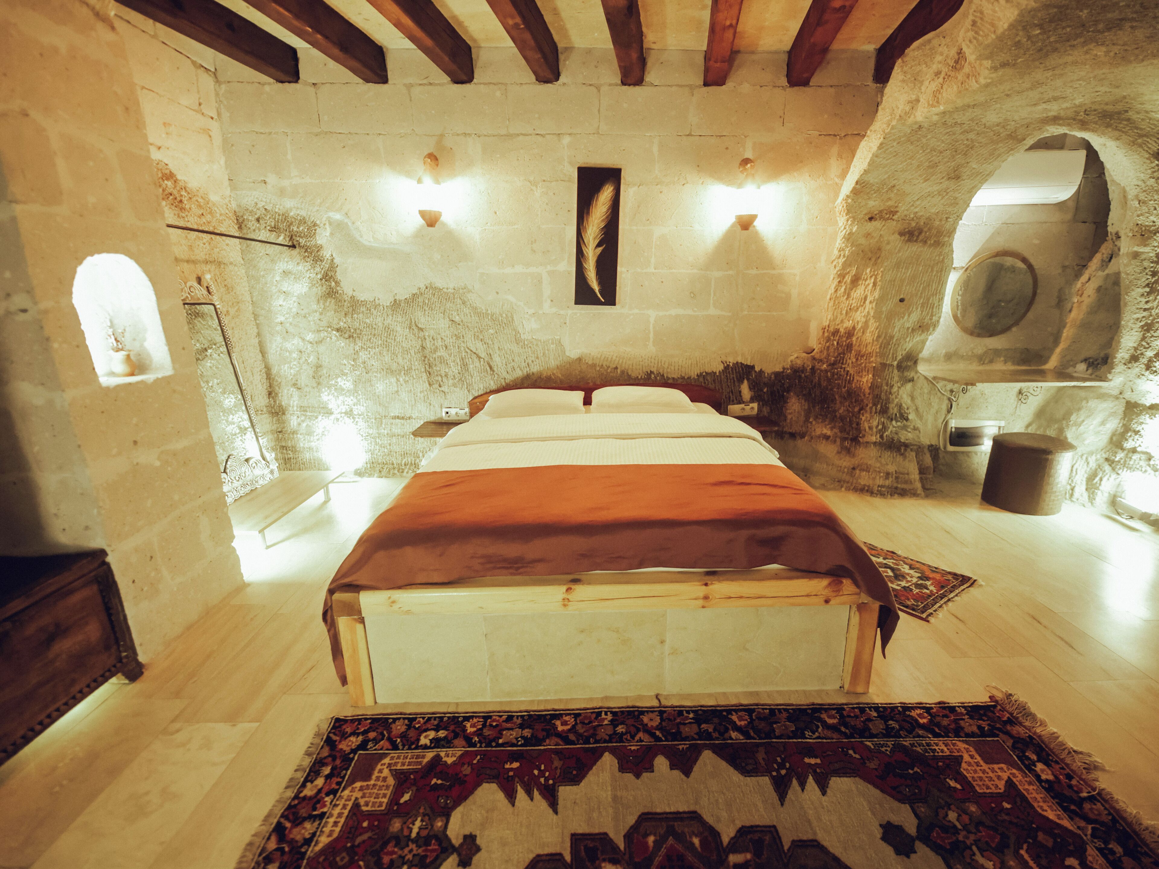 A rustic stone-walled room with a wooden bed, a small table, and a rug.