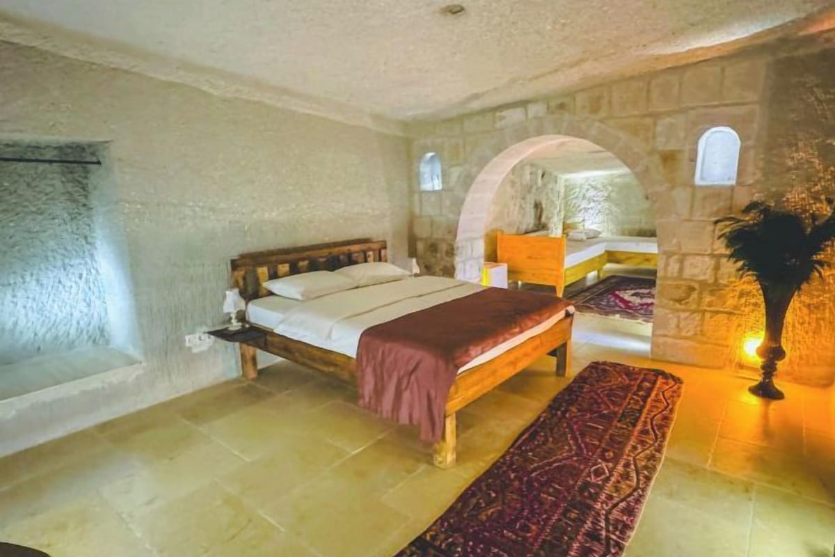 A bedroom with a bed, a bench, a stone wall, and a window.