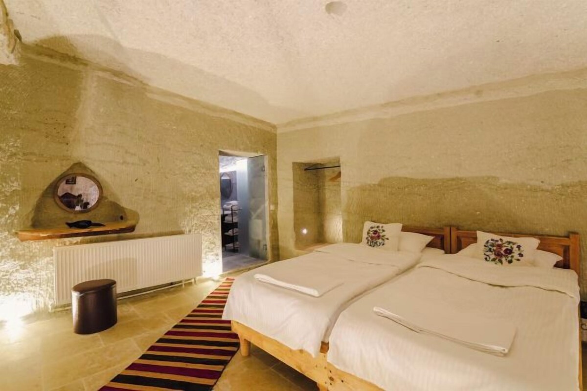 A rustic bedroom with a stone wall, a wooden bed with white bedding, a small round table, and a radiator.